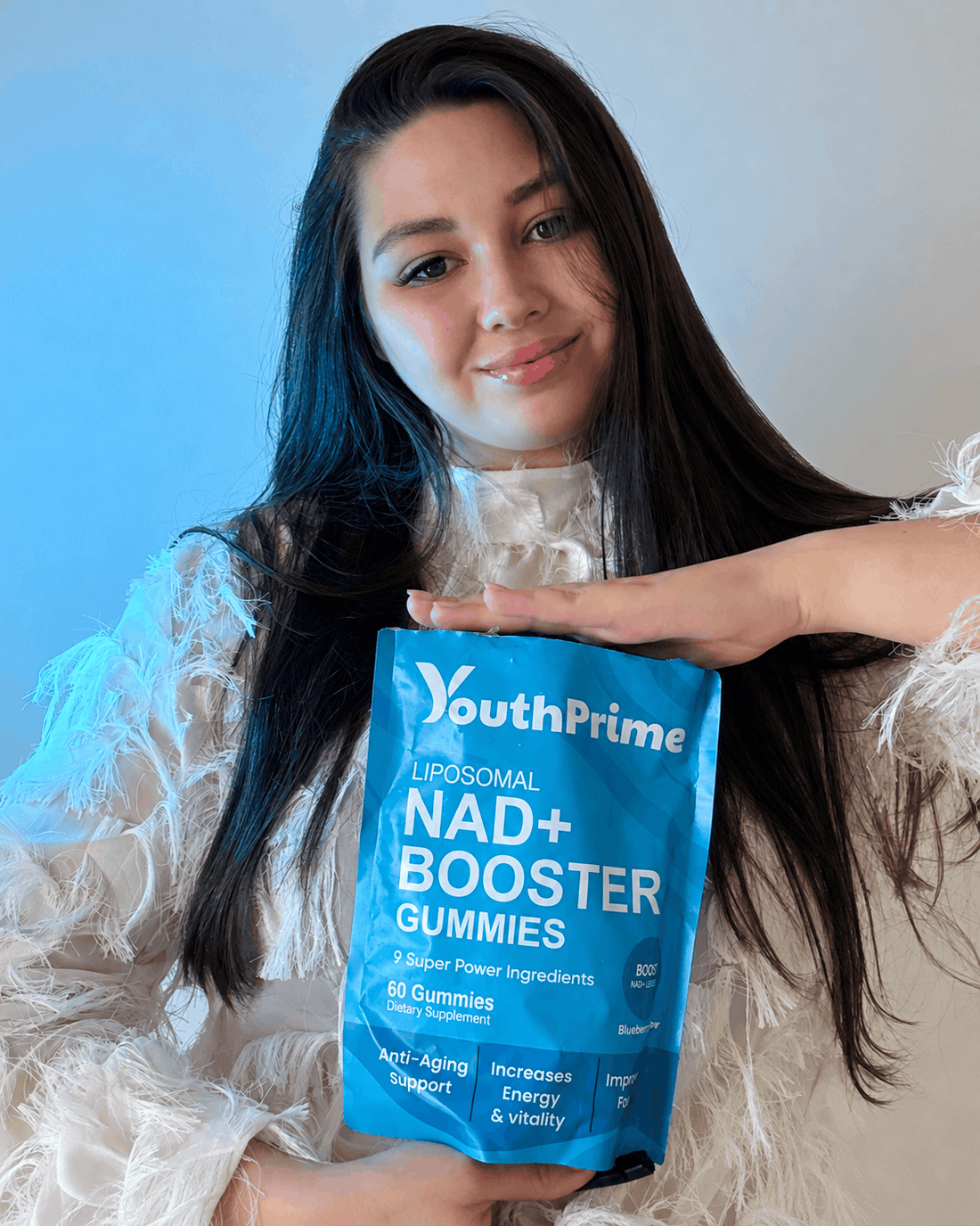 A smiling woman holds the blue YouthPrime NAD+ Booster Gummies pouch